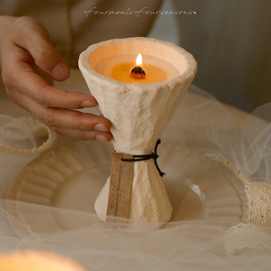 Hand placing a lit Four Meals Four Seasons sculptural candle on a plate in a warm interior