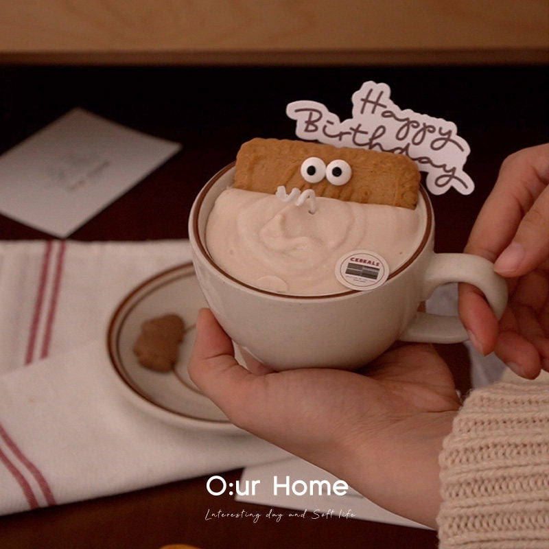 Hands holding the Caramel Oat cup-and-saucer candle in a warm interior