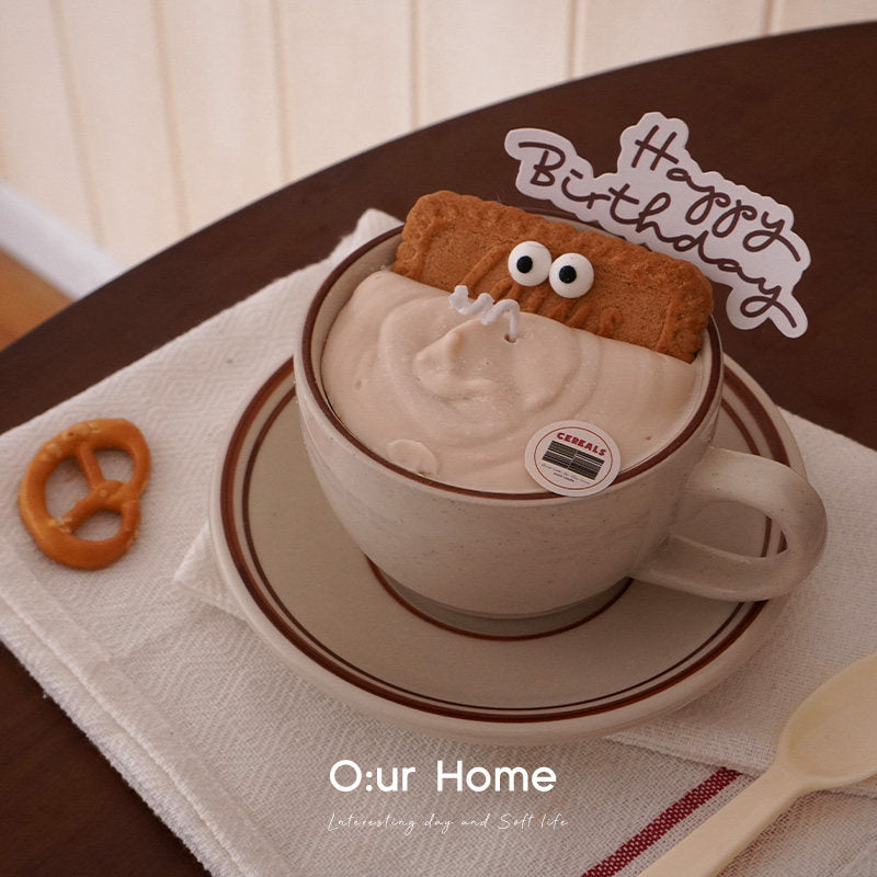 O:urHome Caramel Oat cup candle styled on a dark wood table with a birthday topper