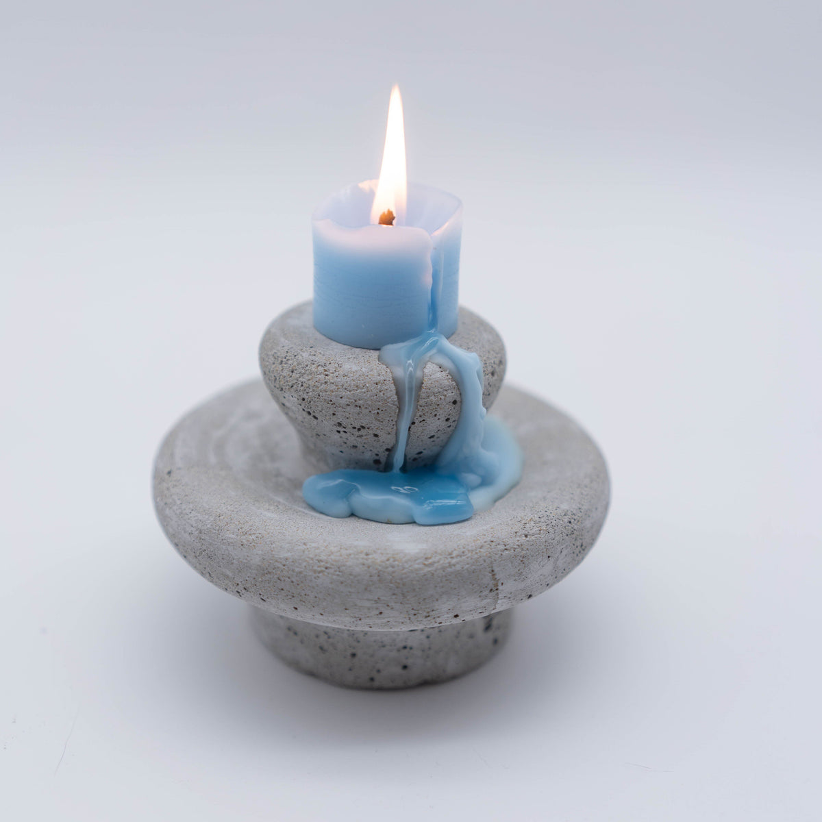 Lit Moon Spring blue sculptural candle with melted wax on a speckled stone base