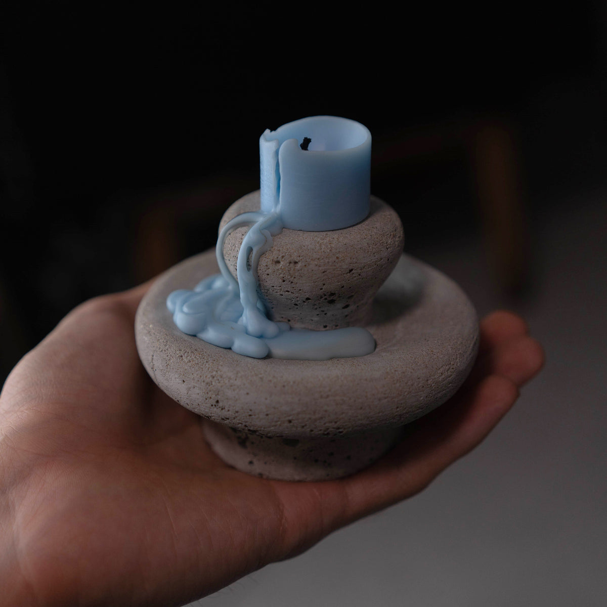 Hand holding the unlit Moon Spring sculptural candle in a dark interior