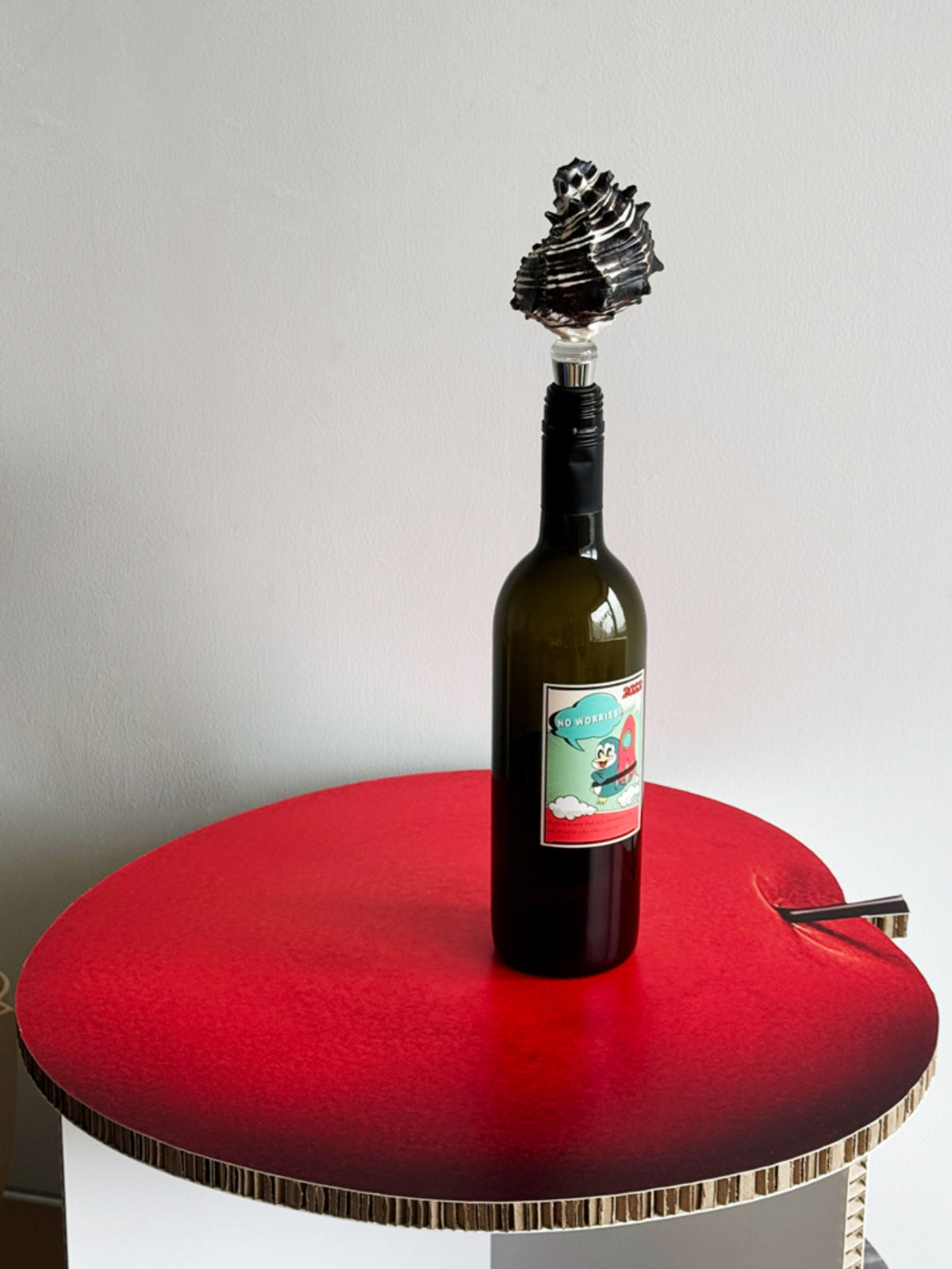 Dark sculptural seashell wine stopper in a bottle on a red side table