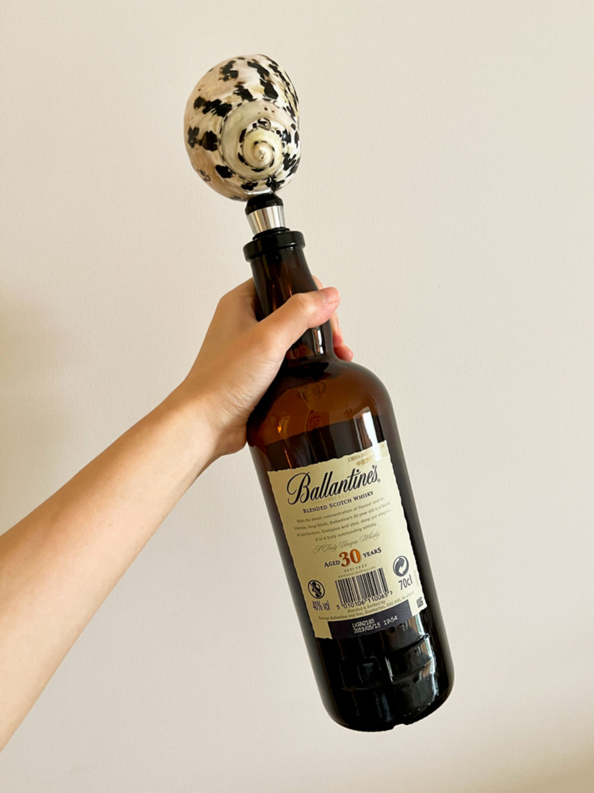 Hand holding a wine bottle fitted with a black-and-white natural seashell stopper