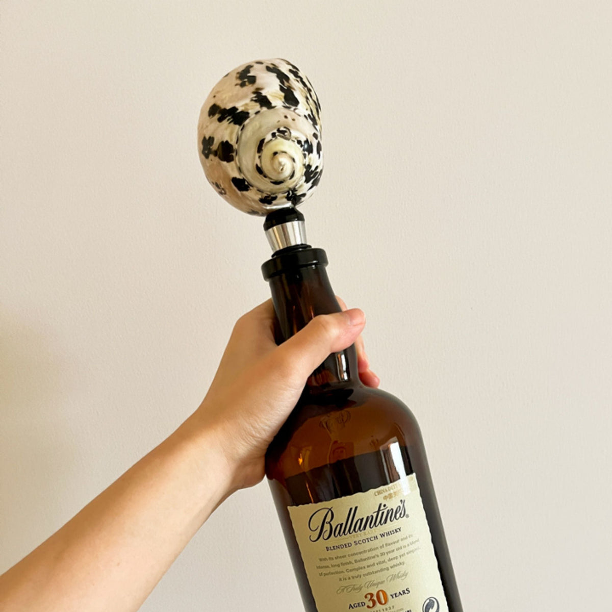 Hand holding a wine bottle fitted with a spotted seashell stopper