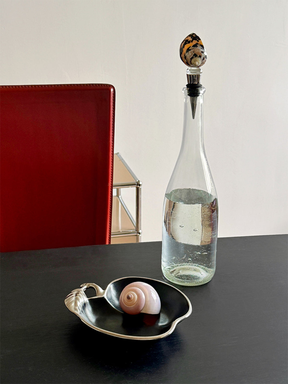 Spotted seashell wine stopper in a clear bottle beside loose shell stoppers