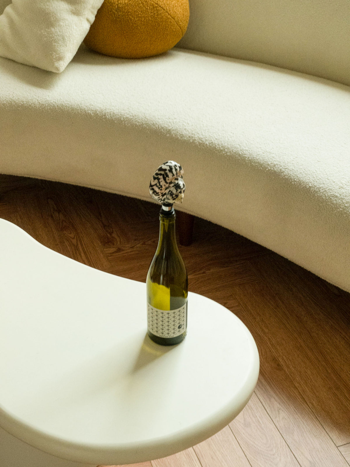 Seashell wine stopper in a bottle on a white side table by a curved sofa
