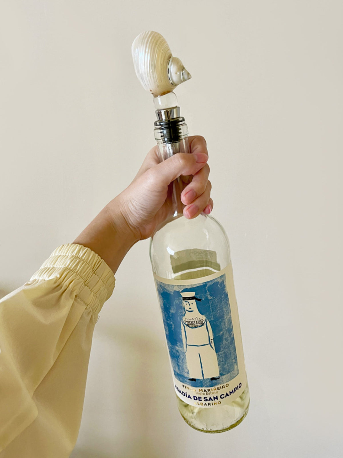 Hand holding a clear bottle fitted with a white ridged seashell stopper