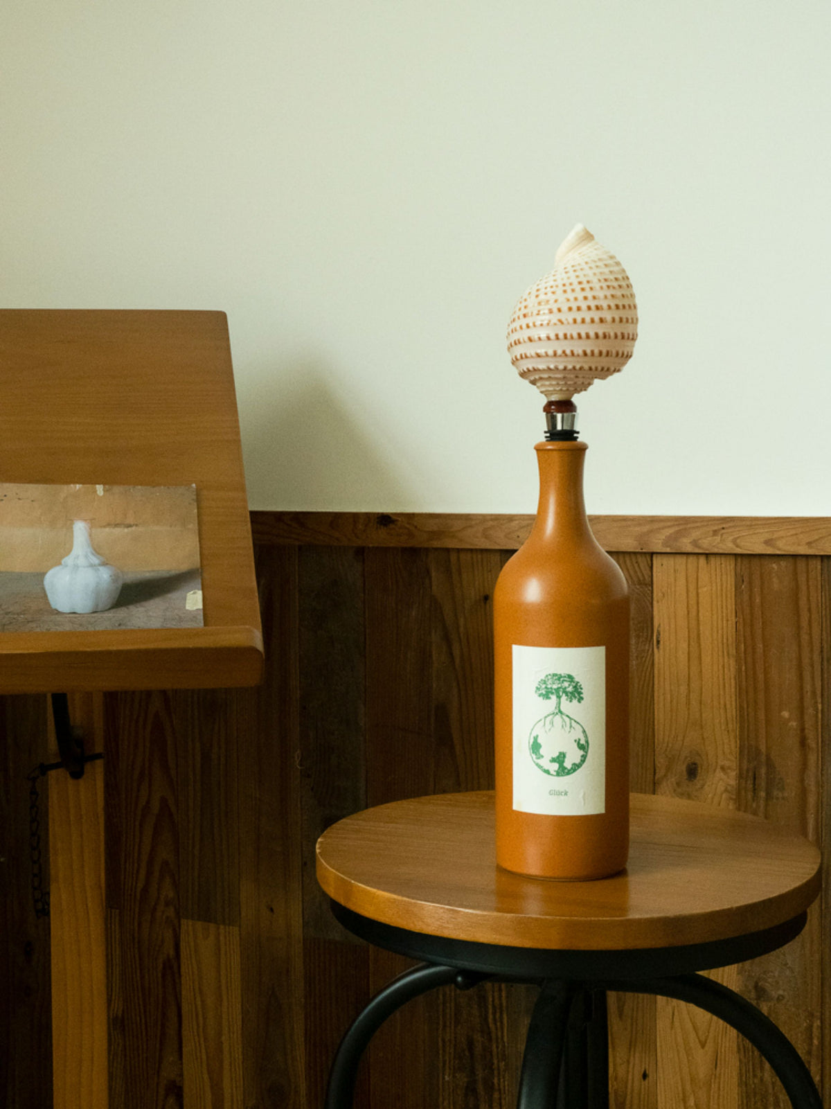 Cream seashell wine stopper in an amber bottle on a wooden stool