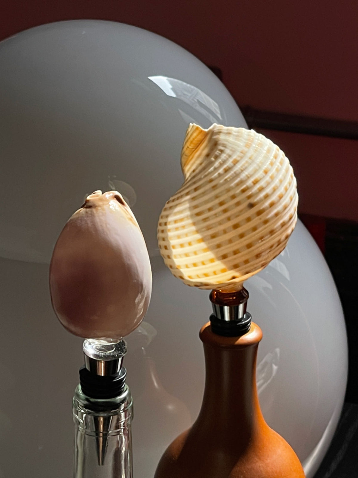 Two natural seashell wine stoppers displayed in glass and amber bottles by a mirror