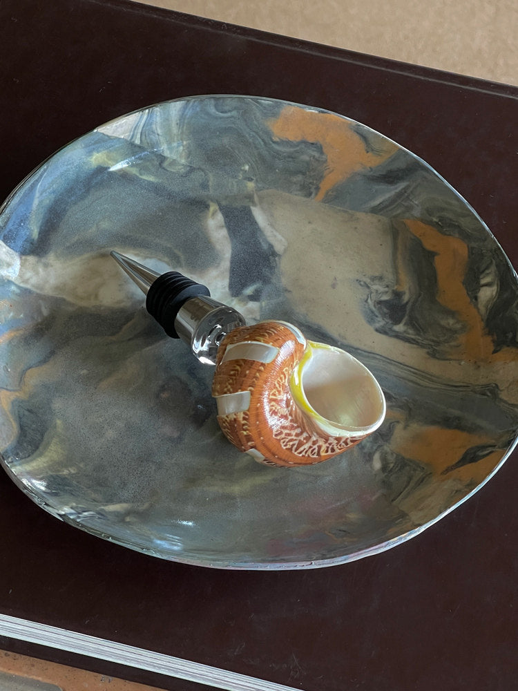 Amber shell wine stopper lying on a reflective glass dish