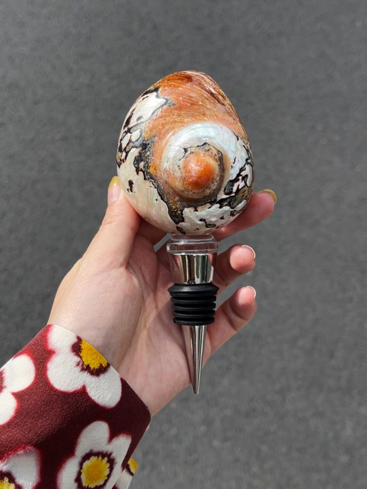 Hand holding an orange-and-cream spiral seashell wine stopper