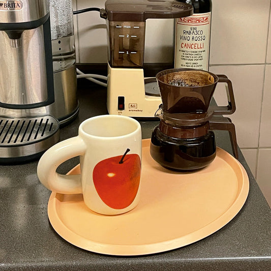 SoftServe red apple ceramic mug beside a coffee brewer on a peach tray
