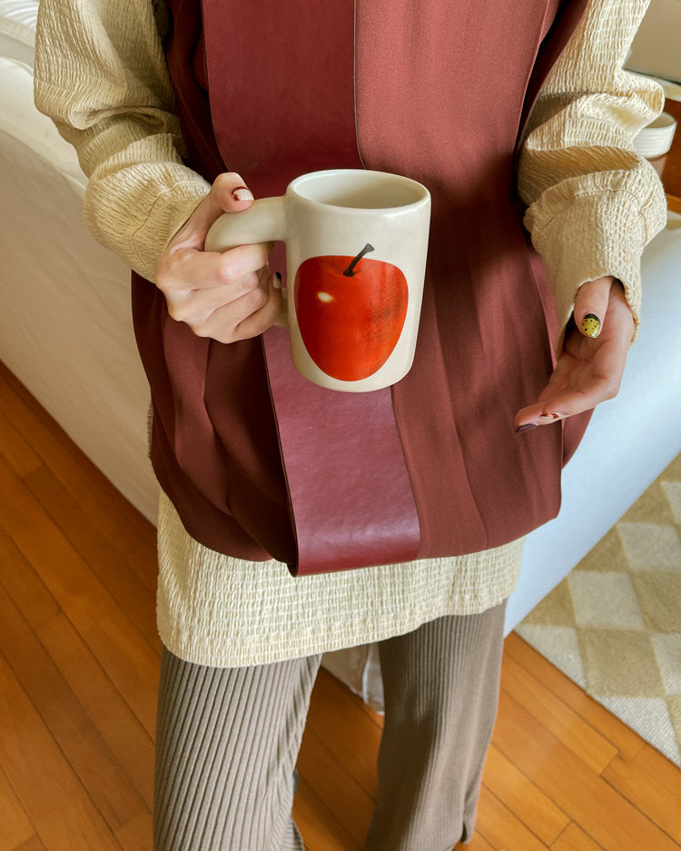 Person holding a SoftServe red apple ceramic mug against a red apron
