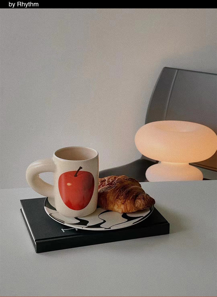 SoftServe red apple ceramic mug beside a pastry and small table lamp