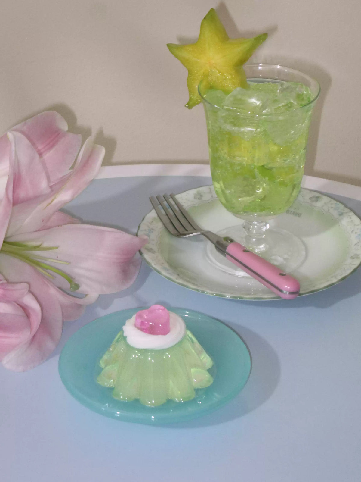 Green HollyJelly pudding candle styled beside a drink and flowers