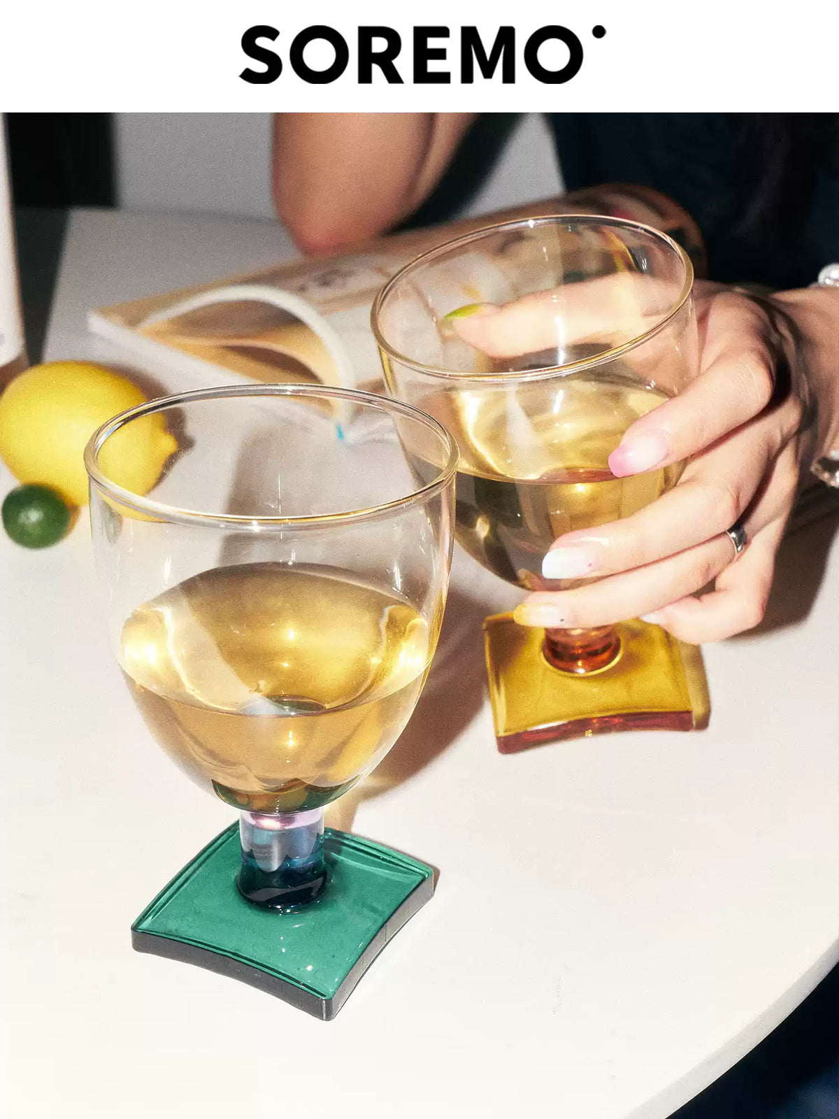 Two SOREMO Sugar Cube colored goblets held at a gathering